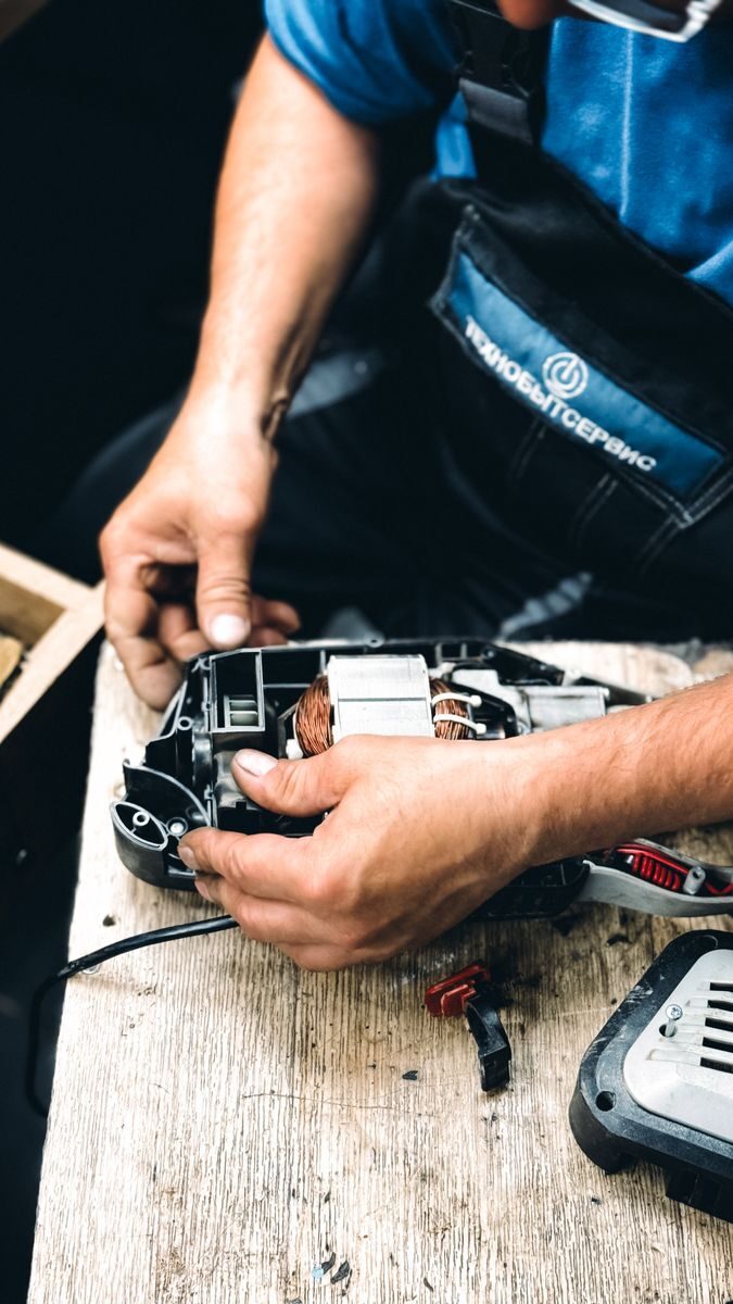 Technician manually fixing an electric tool on a wooden surface.