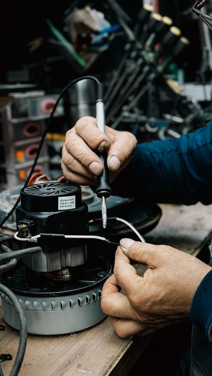 A person skillfully soldering components in a workshop filled with tools and equipment.